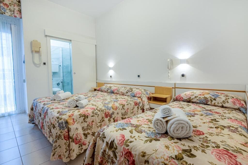 Habitación de hotel con dos camas, un baño y una puerta de vidrio que da a un balcón.