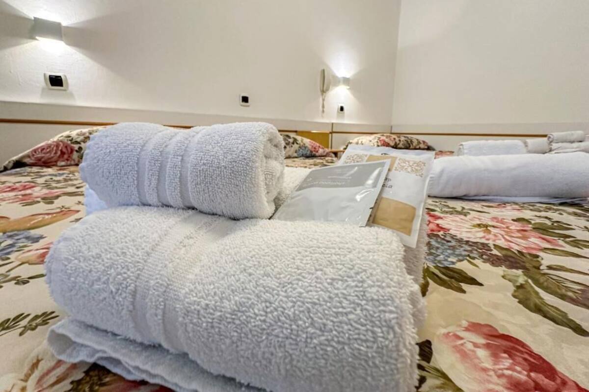 A hotel room with a bed, multiple towels, a floral bedspread, and a wall-mounted light fixture.