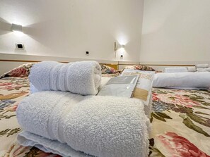 A hotel room with a bed, multiple towels, a floral bedspread, and a wall-mounted light fixture. - Hotel Ilde (Rimini)