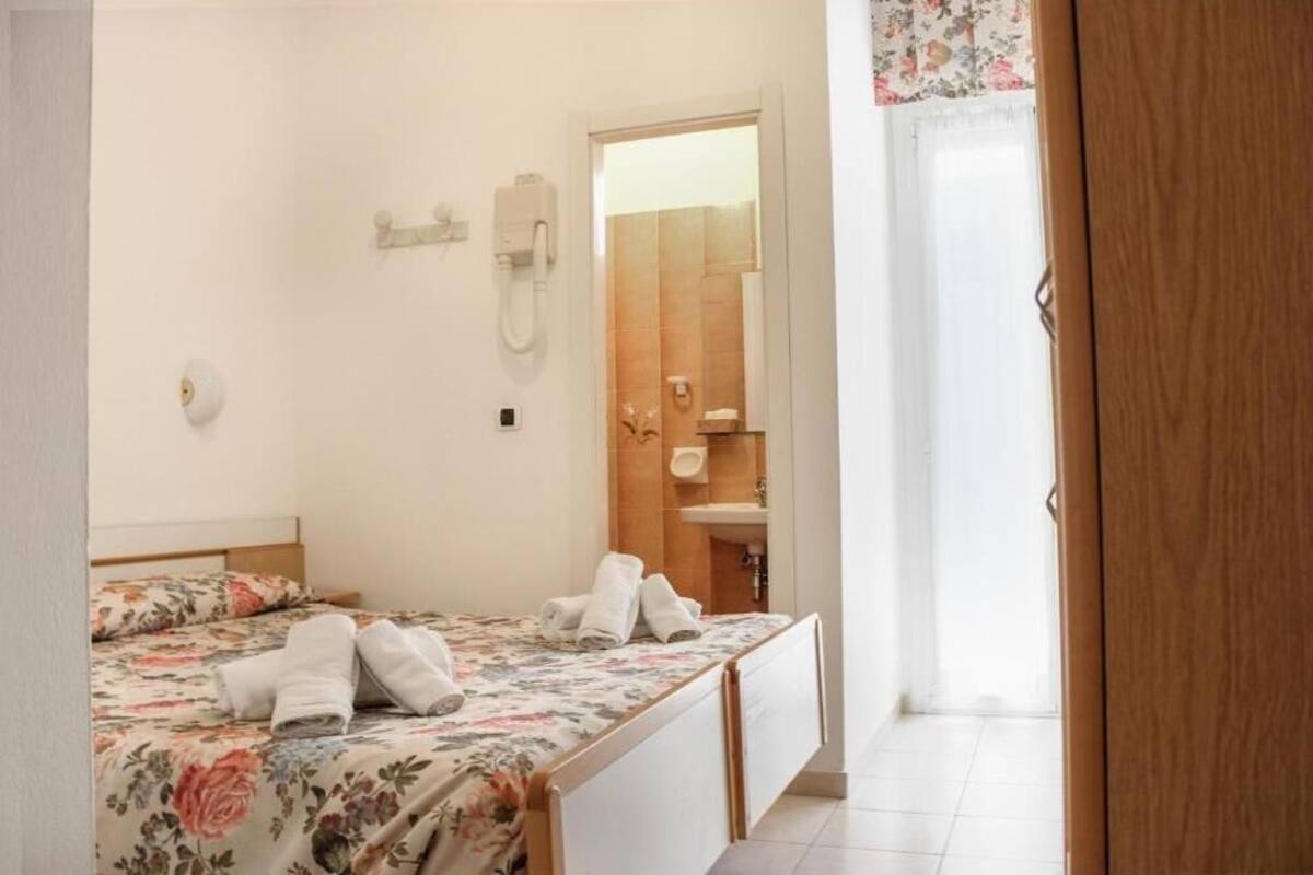 A bedroom with a bed, a bedside telephone, and a bathroom visible through an open door.