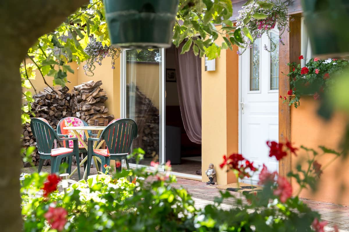 Une terrasse extérieure avec une table et des chaises, une pile de bois de chauffage et une porte donnant sur un espace intérieur.