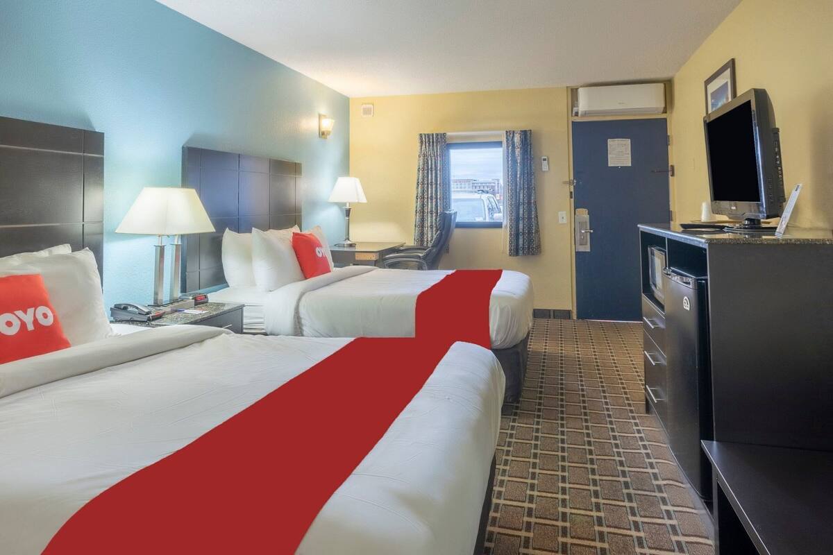 Una habitación de hotel con dos camas, un escritorio, un televisor y una ventana con cortinas.