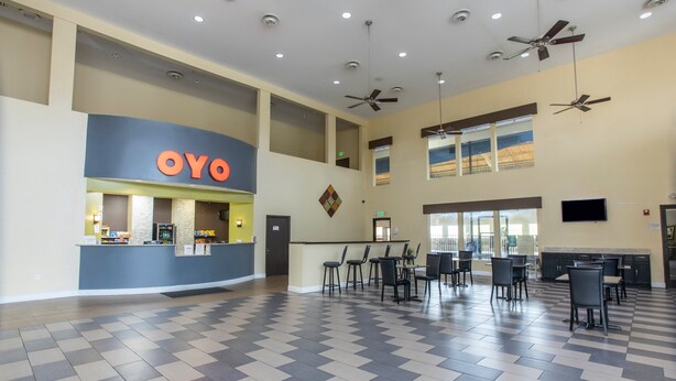 Un vestíbulo amplio con mostrador de recepción identificado como 'OYO', varias zonas de estar y ventiladores de techo.