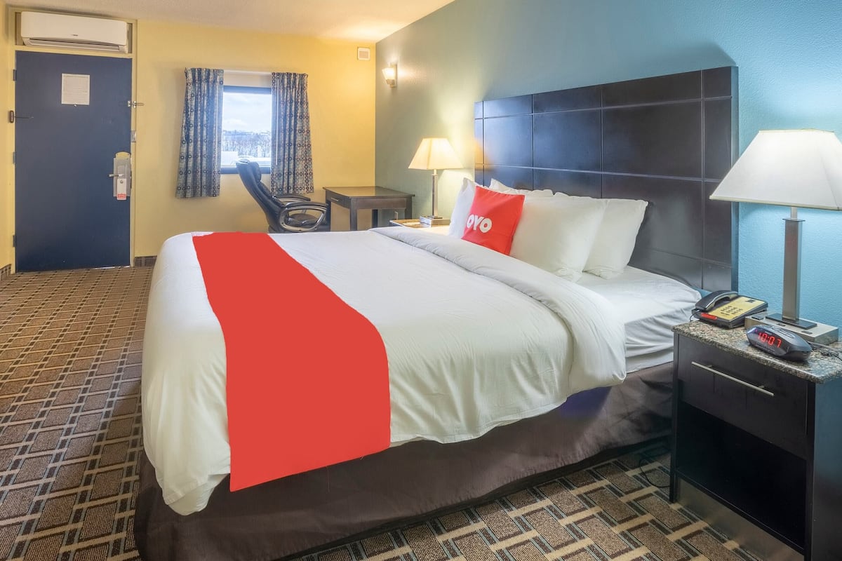 Habitación de hotel con cama, mesita de noche con lámpara, una silla y ventana con cortinas.