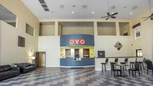 Un vestíbulo de hotel con una recepción identificada como 'OYO', un mostrador de check-in, una zona de estar con sillas y mesas, y un suelo estampado.