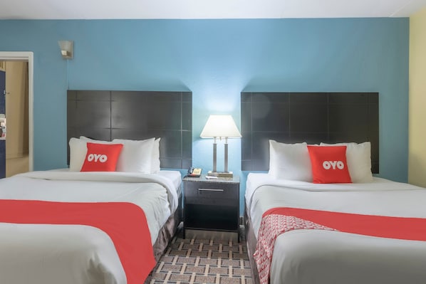 Habitación de hotel con dos camas, cada una con un cojín rojo 'OYO', una mesita de noche con lámpara y suelo estampado.
