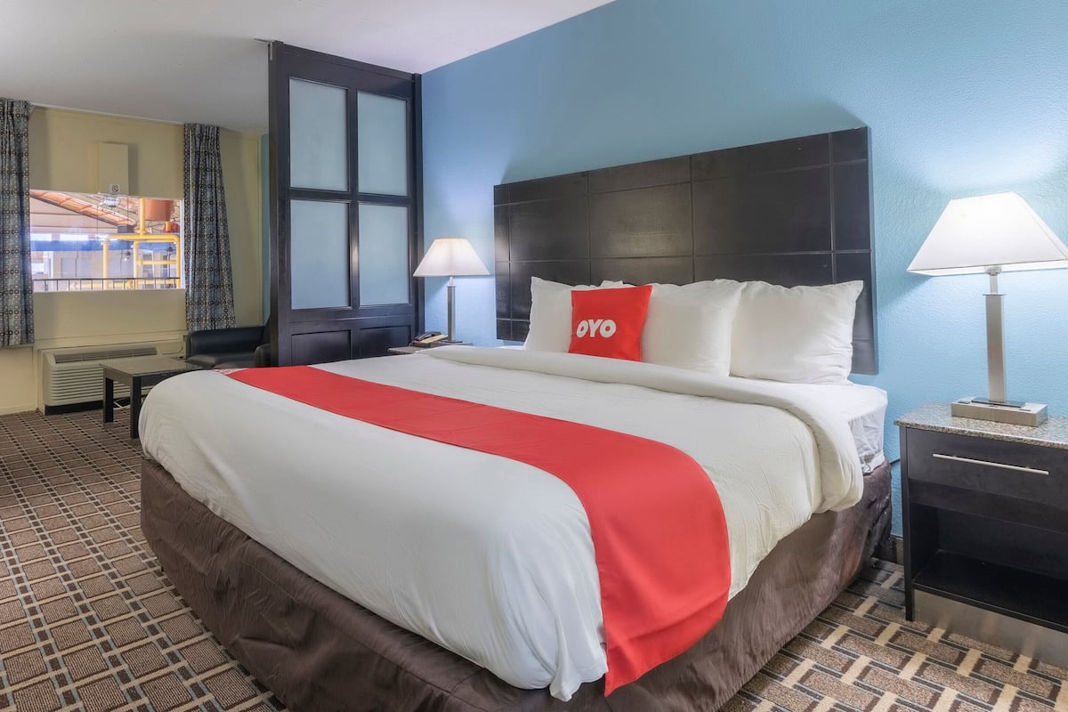 Habitación de hotel con una cama grande, dos lámparas de noche, una mesita de noche y una ventana con cortinas.