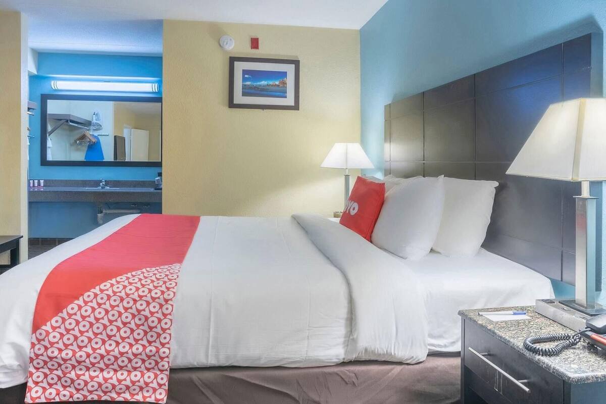 Una habitación de hotel con una cama, una mesita de noche, una lámpara, un espejo y un cuadro en la pared.