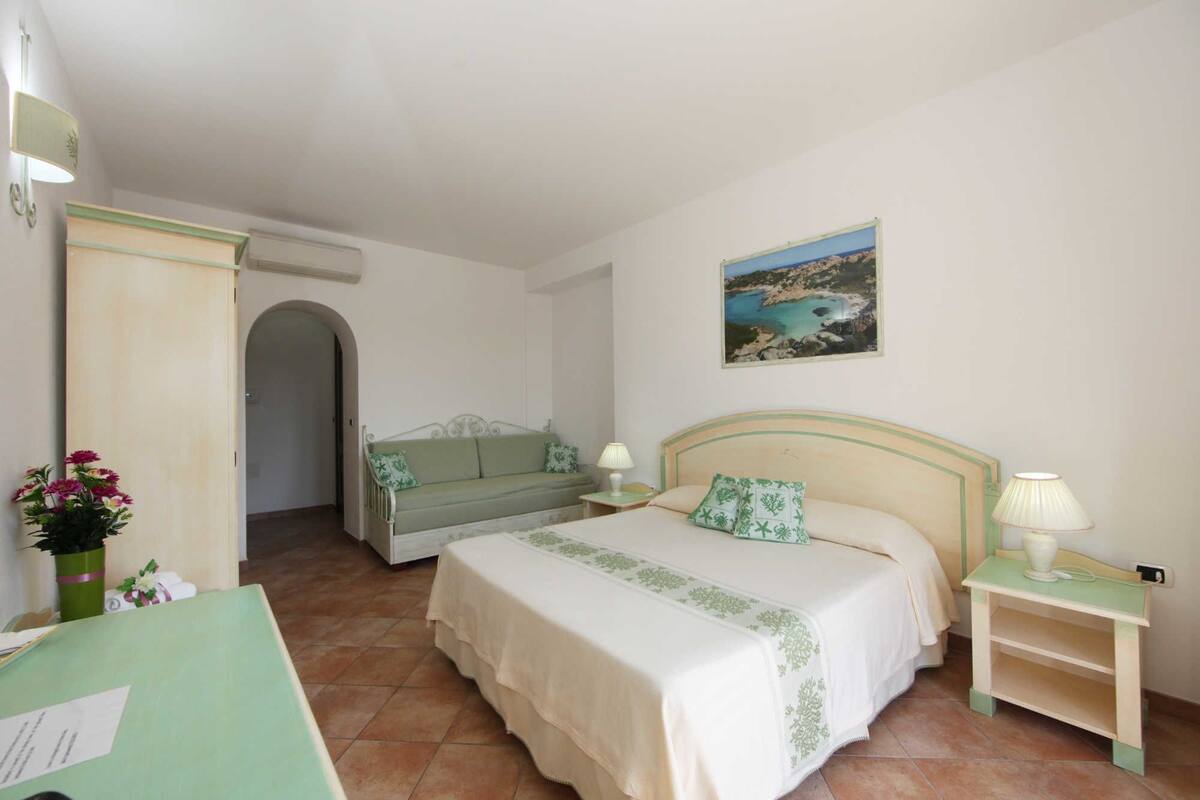 Une chambre à coucher avec un lit, une table de chevet, une chaise, un bureau et un tableau accroché au mur.