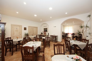 A spacious dining area with multiple tables and chairs, featuring a tiled floor and white walls. - Guest House Villabianca (La Maddalena)