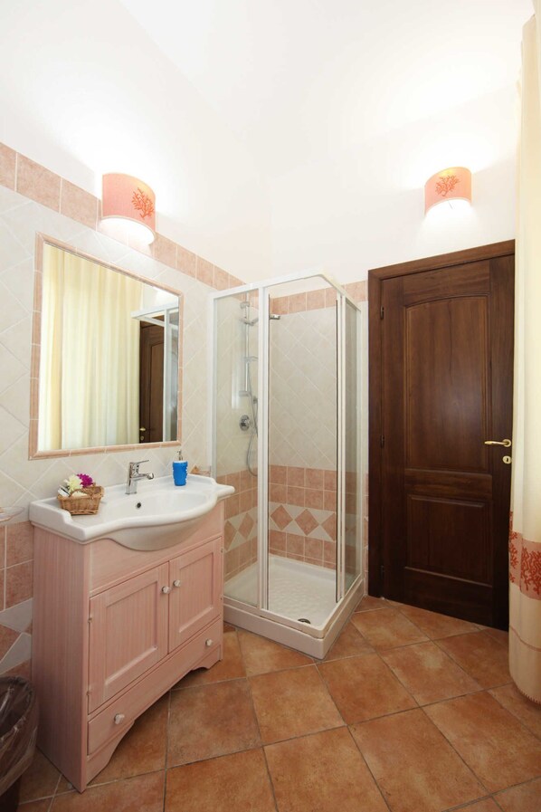 A bathroom with a sink, mirror, shower, and a wooden door. - Guest House Villabianca (La Maddalena)