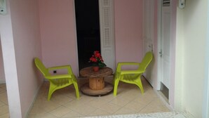 Ein kleiner Patio-Bereich mit zwei grünen Plastikstühlen, einem Holztisch und einem Blumentopf.