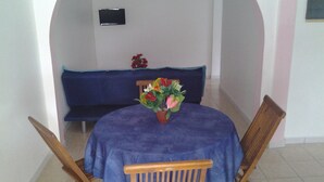 Ein Essbereich mit einem runden Tisch, der mit einer blauen Tischdecke bedeckt ist, zwei Holzsesseln, einer Bank und einem Blumentopf mit Blumen.