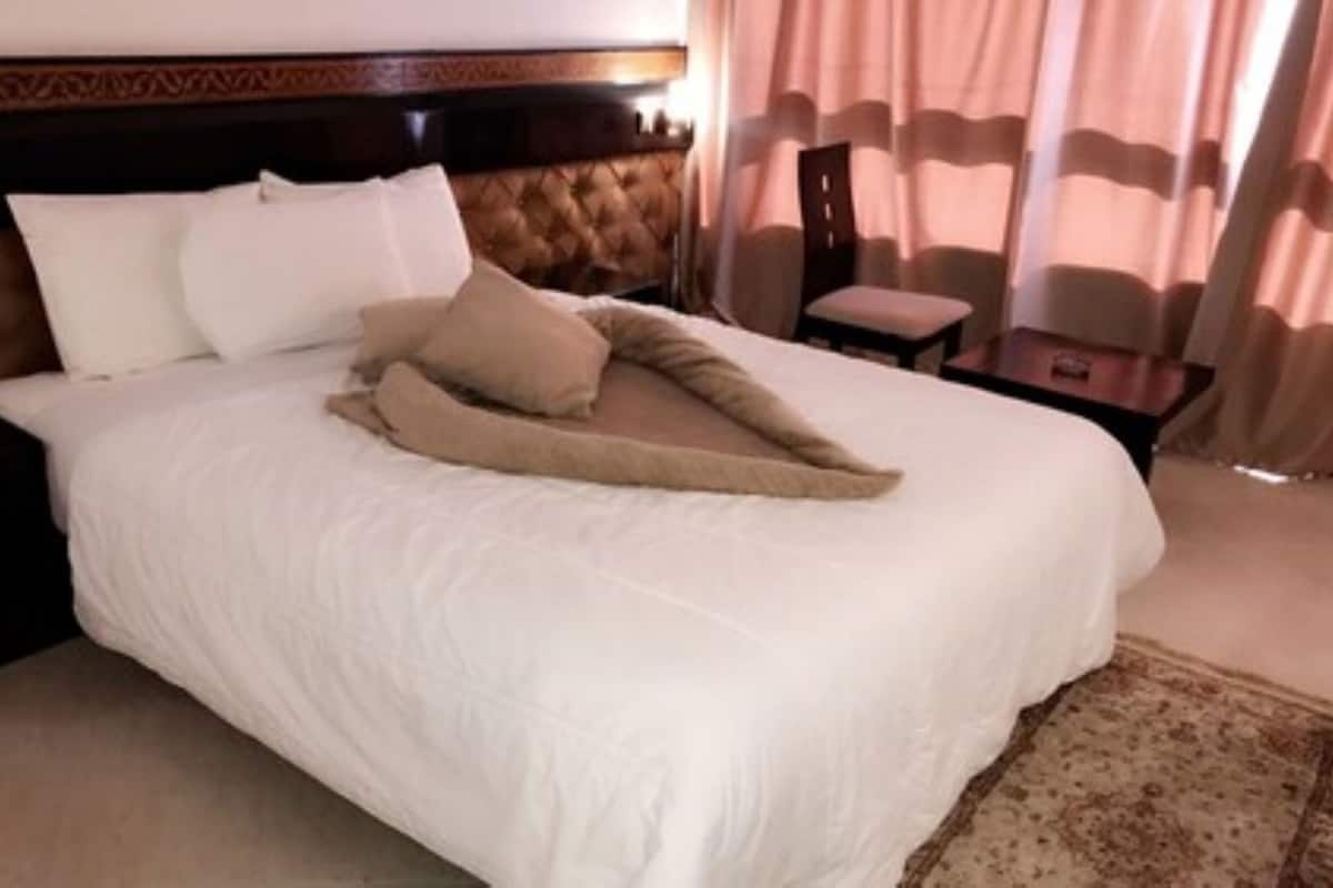 A hotel room with a large bed, a wooden headboard, a small table, and a chair.