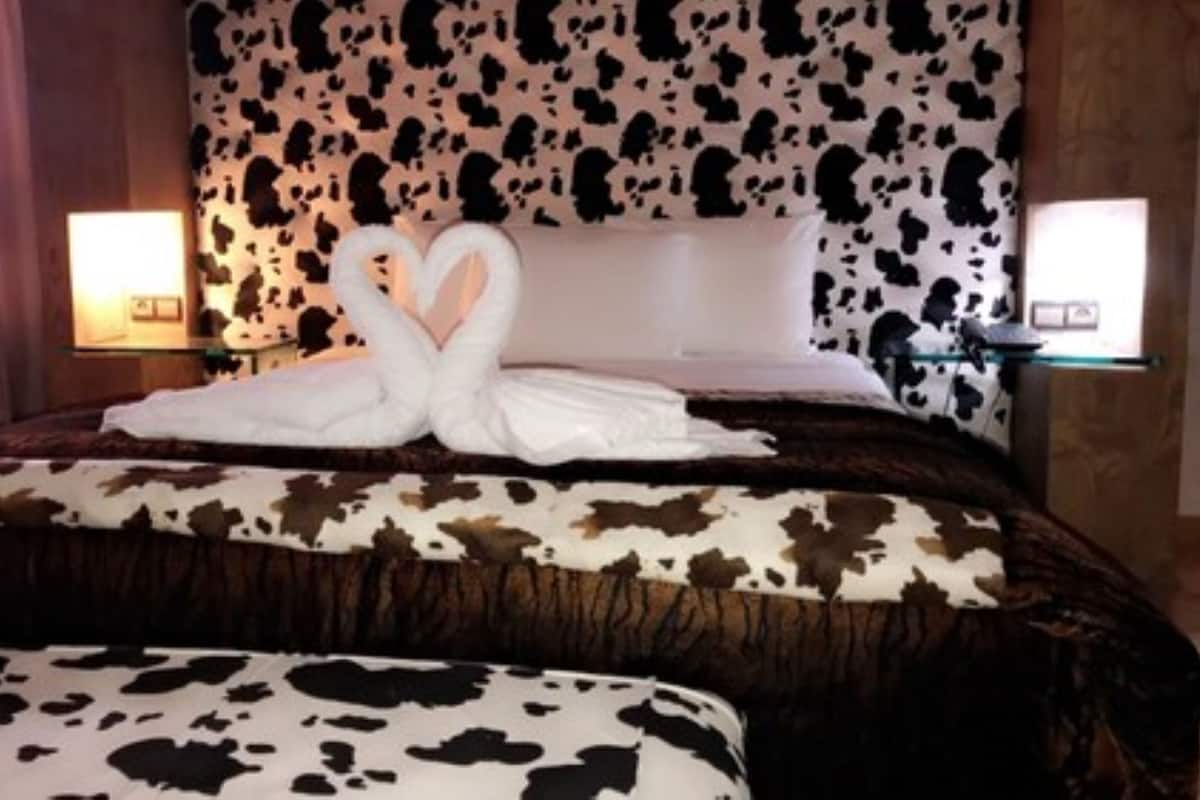 A bed with a cow print bedspread and pillows, two bedside tables with lamps, and a cow print headboard.