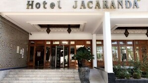 L’entrée de l’hôtel Jacaranda, avec sa façade en pierre, ses portes en bois et un grand pot de fleurs placé en premier plan.