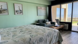 Un dormitorio con cama, sofá, mesa de centro y un amplio ventanal con persianas.