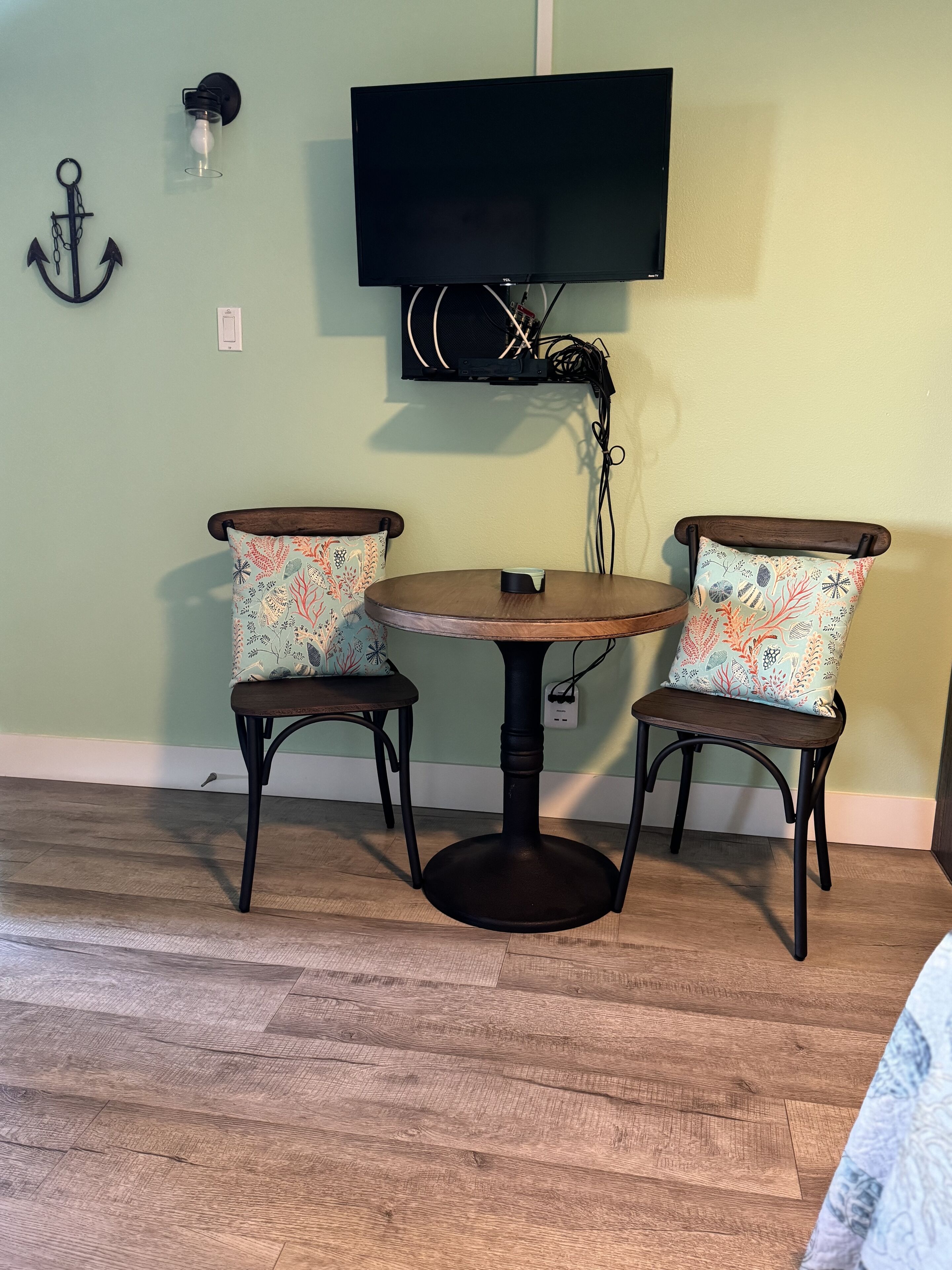 Een eethoek met een ronde tafel en twee stoelen, een tv aan de muur en een decoratieve anker.