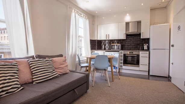 Un espace de vie compact comprenant un canapé, une table à manger, des chaises, un coin cuisine et un réfrigérateur.