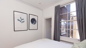 Une chambre à coucher avec un lit, une fenêtre avec des rideaux et deux tableaux encadrés accrochés au mur.