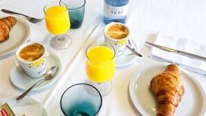 Une table mise pour le petit-déjeuner, avec des croissants, des tasses de café et des verres de jus d’orange, le tout posé sur une nappe blanche.