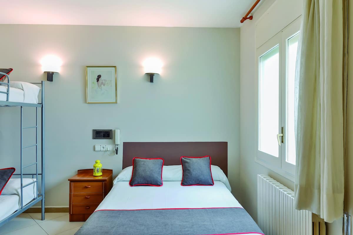 A hotel room with a bunk bed, a bedside table with a lamp, a framed picture on the wall, and a window with curtains.