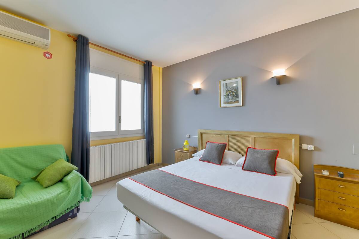 A hotel room with a bed, a green sofa, a nightstand, and a wall-mounted light fixture.