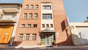Un hôtel à la façade en briques, avec une entrée centrale surmontée d’un auvent incurvé et une enseigne indiquant son nom.
