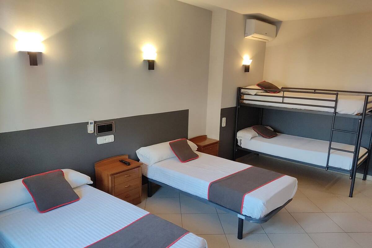 A hotel room with two single beds, a bunk bed, a bedside table with a phone, and wall-mounted lights.
