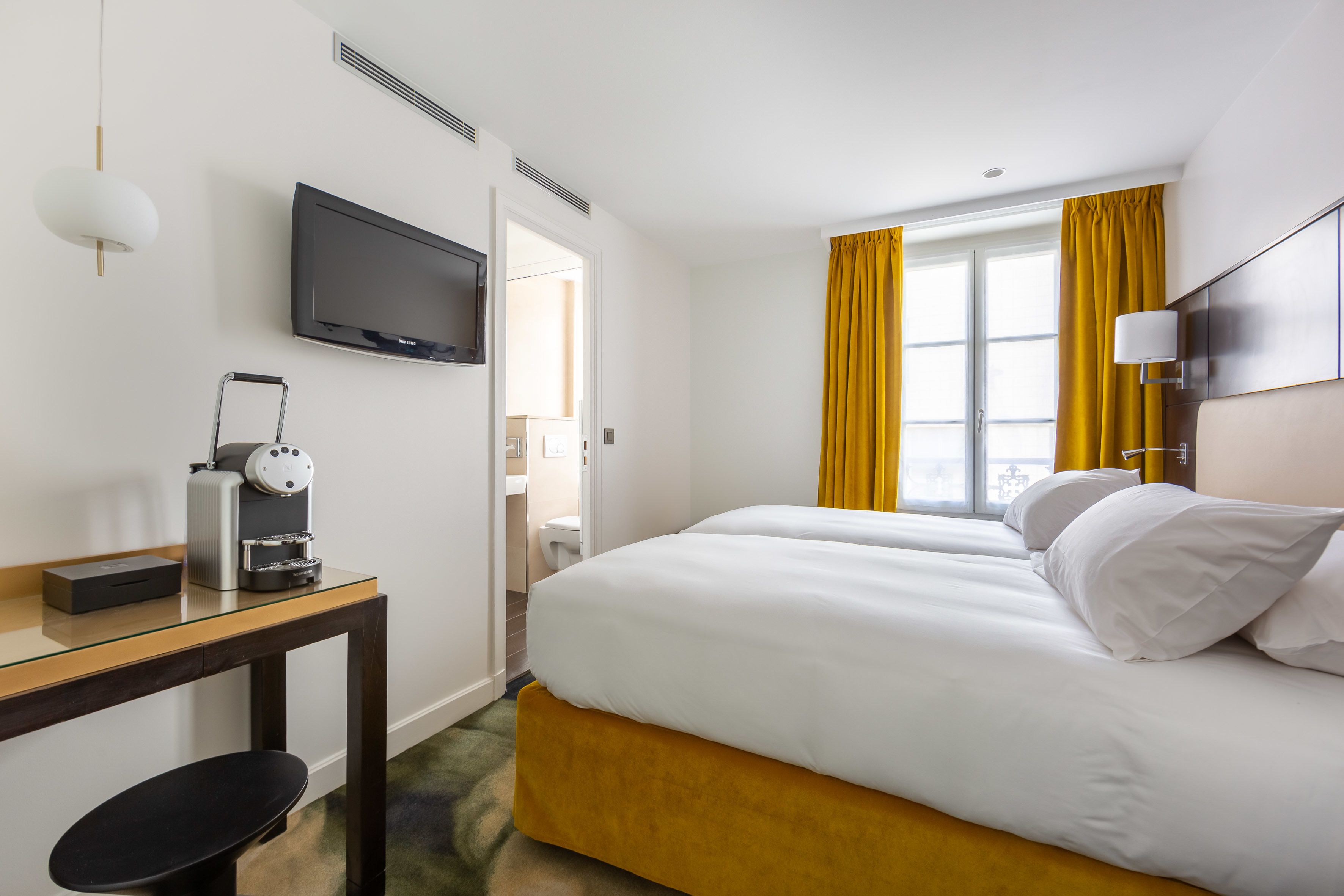 Une chambre d’hôtel équipée d’un lit, d’une télévision, d’une machine à café et d’une fenêtre avec des rideaux.