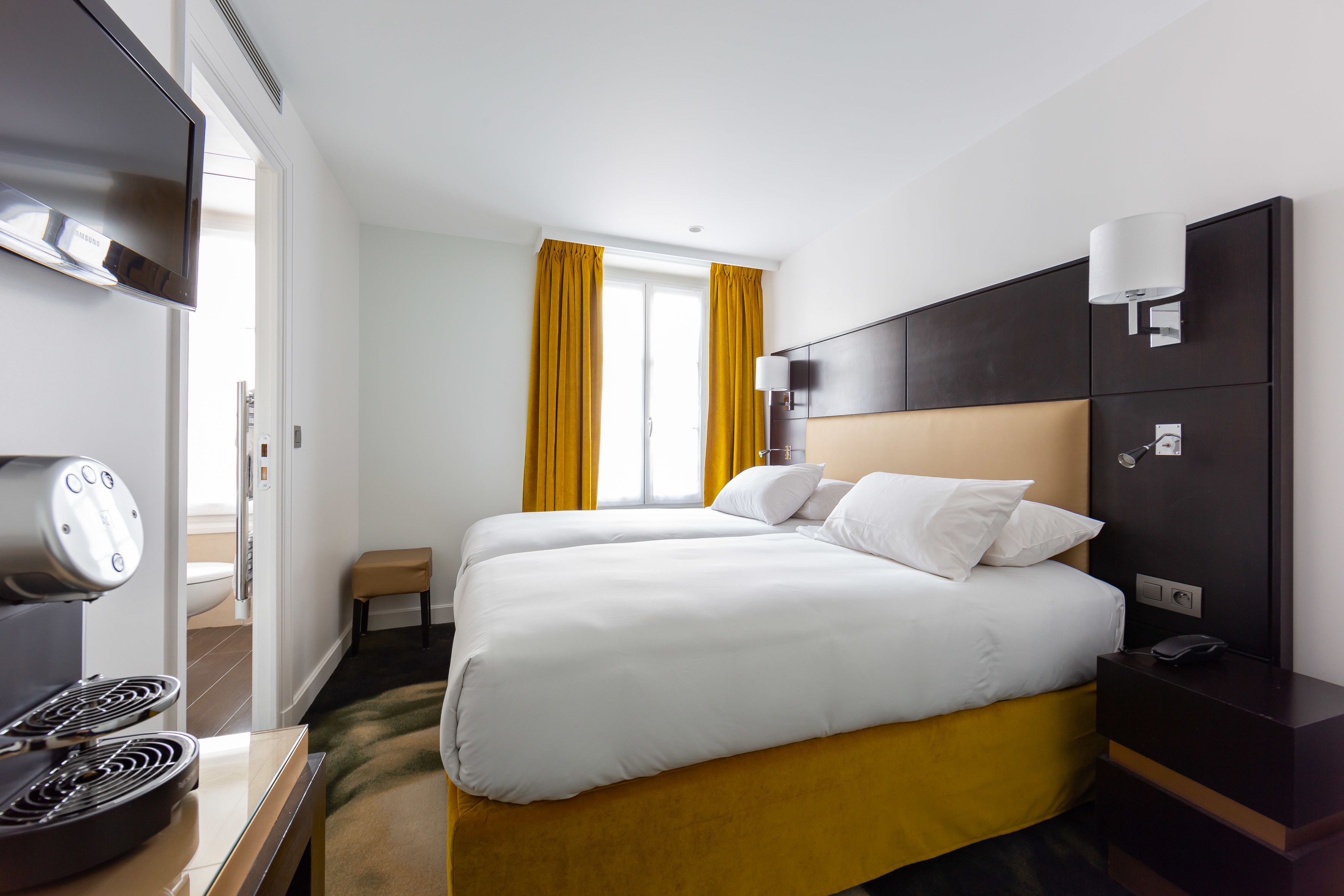 A hotel room with a bed, a TV, a coffee machine, and a window with curtains.