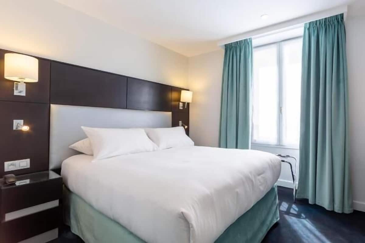 A hotel room with a bed, a desk, a lamp, and a window with curtains.
