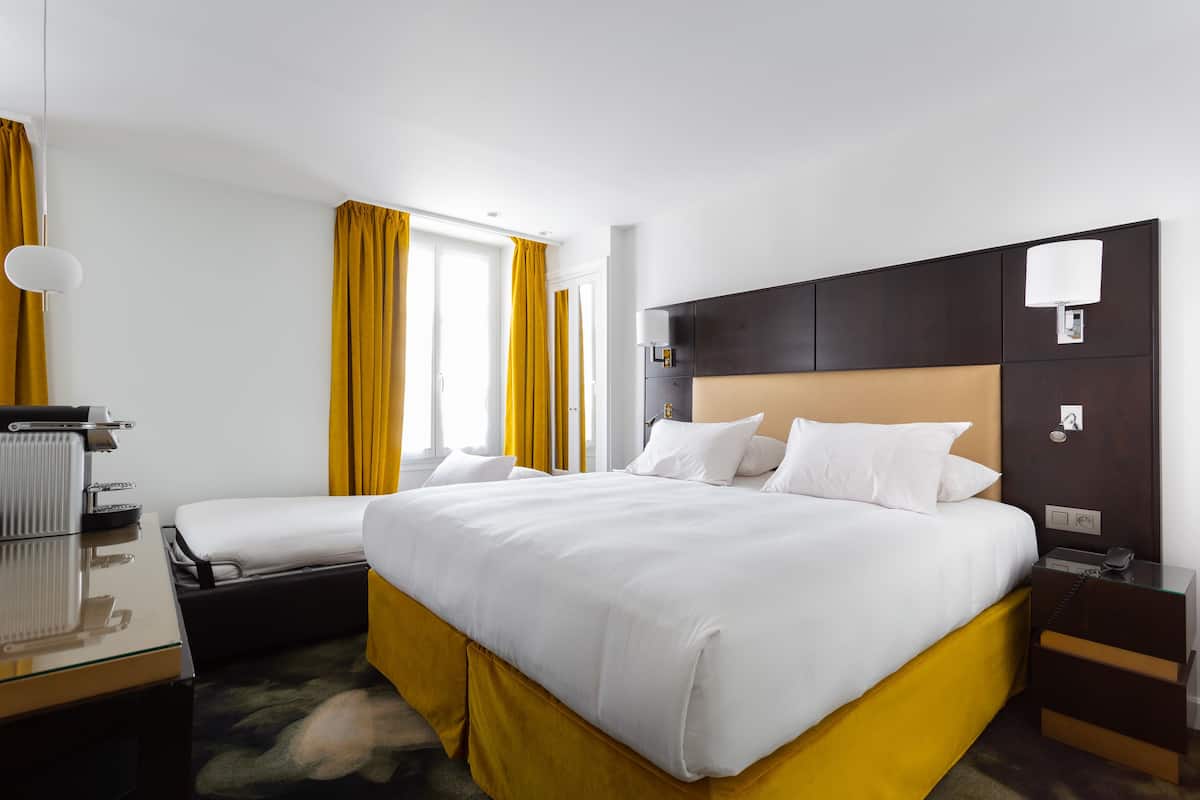 A hotel room with a large bed, a bedside table, a lamp, and a window with curtains.