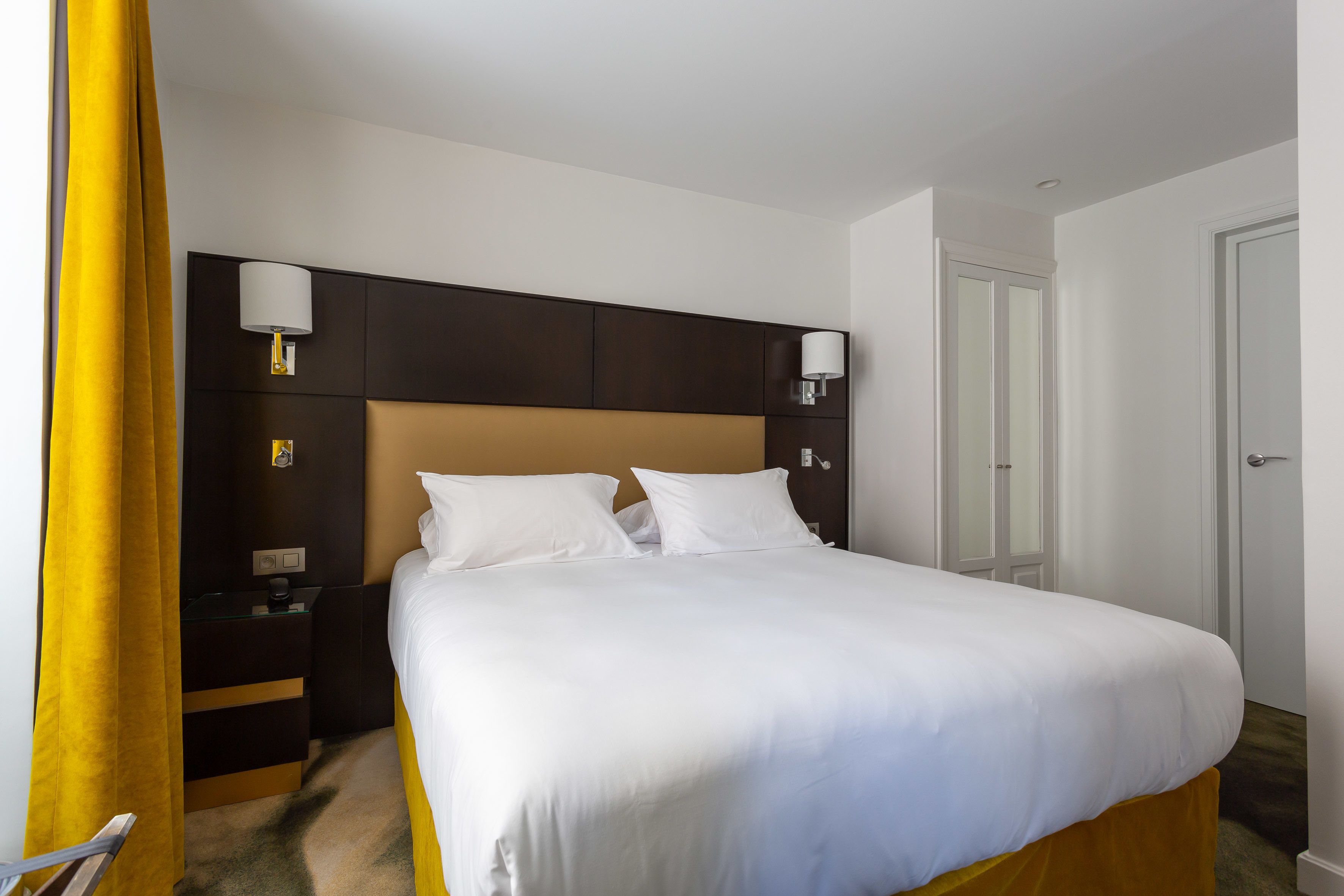 A hotel room with a large bed, two bedside tables with lamps, a wardrobe, and a door.