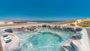 A hot tub with a clear view of the ocean and a rocky landscape in the background.