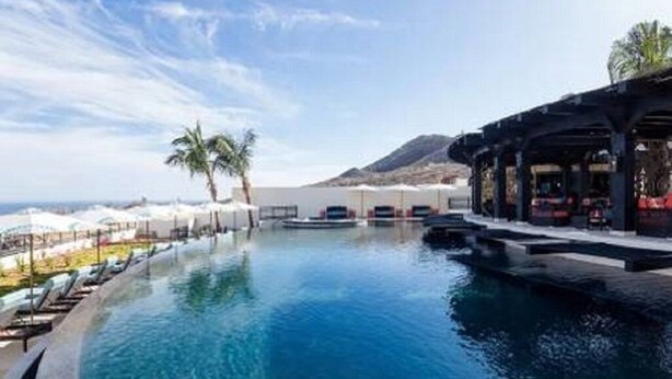 A pool with lounge chairs and umbrellas, a palm tree, and a mountain in the background.