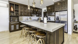 A modern kitchen with dark wood cabinets, a large island with stools, stainless steel appliances, and pendant lighting.