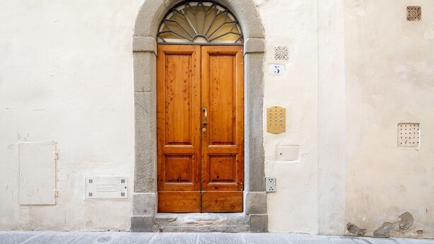 Una puerta doble de madera con un arco de piedra, una pequeña ventana con celosía decorativa y una caja de servicios en la pared.