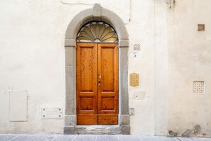 A double wooden door with a stone archway, a small window with a decorative grille, and a utility box on the wall. - Vellutini by Mmega (Florence)