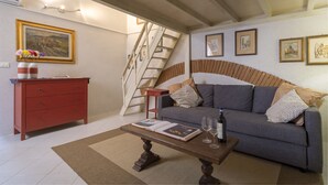 Una sala de estar con un sofá, una mesa de centro con un libro y copas de vino, un aparador rojo y una escalera.