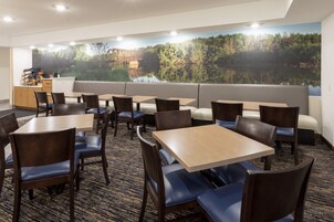Un comedor de hotel con mesas, sillas, un sofá y un gran mural de un bosque y un puente.