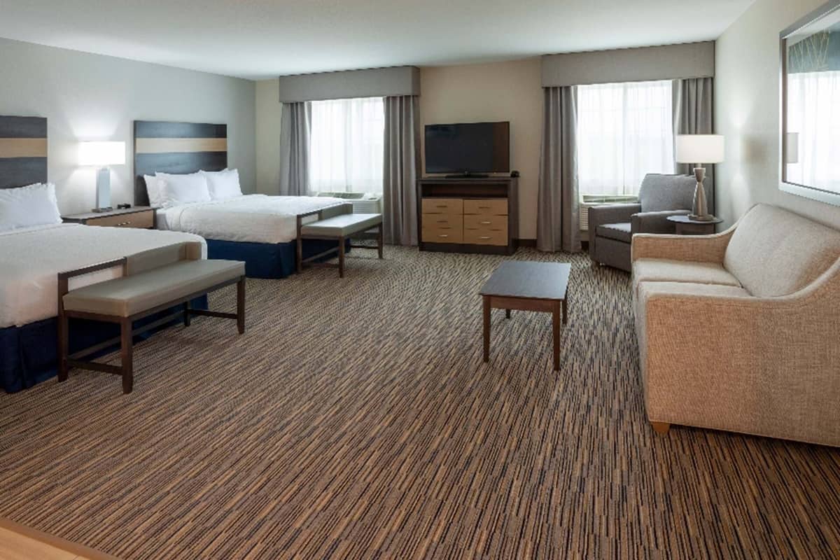 A hotel room with two beds, a sofa, a TV, and a small table.
