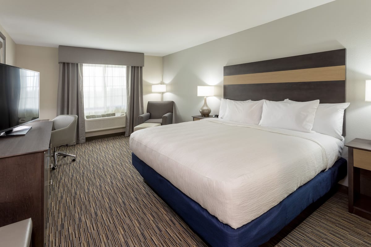 A hotel room with a large bed, a desk, a chair, and two bedside lamps.