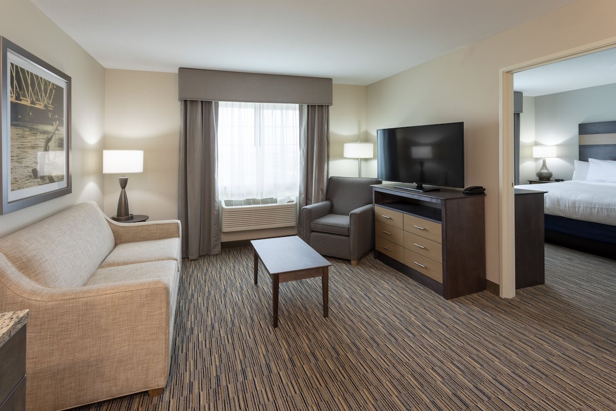A hotel room with a sofa, a small table, a TV, a desk with drawers, and a bed.
