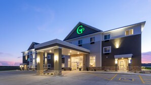Um hotel com vários andares, um logotipo verde bem visível no telhado, entrada coberta e área de estacionamento com acessibilidade para pessoas com deficiência.