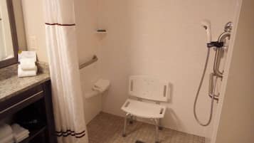 Een kleine badkamer met tegels, een douche, een witte stoel en een handdoekhouder.
