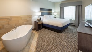 Quarto de hotel moderno com uma banheira grande, uma cama bem arrumada, uma escrivaninha e uma janela ampla com cortinas.