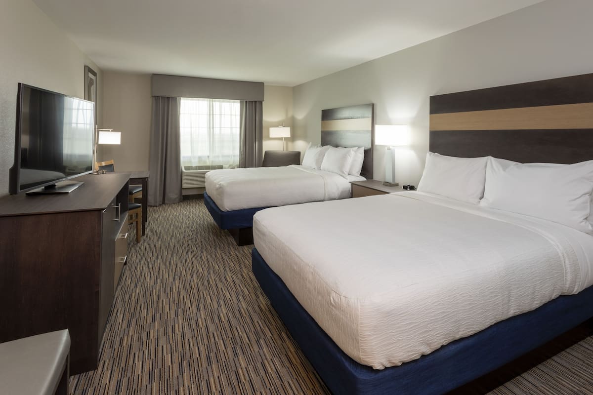 A hotel room with two beds, a desk, a TV, and a window with curtains.