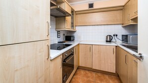 A kitchen with wooden cabinets, a microwave, a kettle, and an oven. - Fitzrovia Apartments by Allô Housing (London)