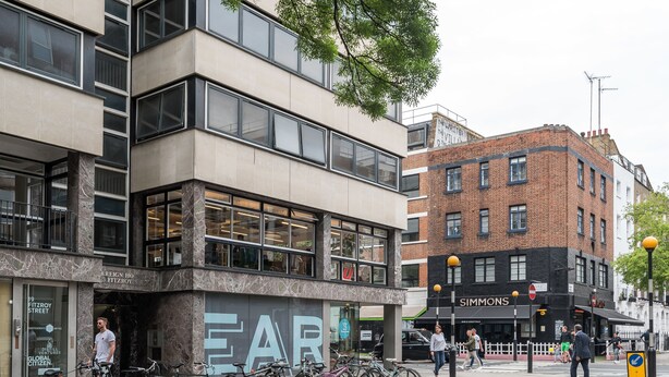 A modern building with a prominent 'EAR' sign, a bike parking area, and a street intersection. - Fitzrovia Apartments by Allô Housing (London)